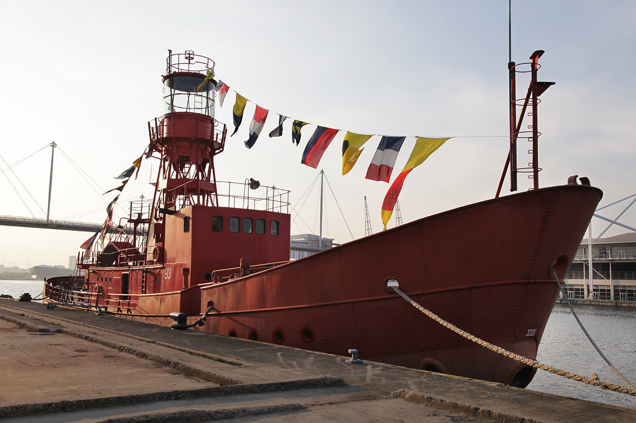 Red boat with lighthouse tower and flags moored on the edge of the dock